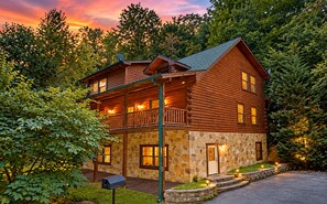 A two-story log cabin with a stone foundation, a balcony, and a stone mailbox.
