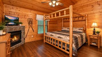A log cabin bedroom with a four-poster bed, a fireplace, a television, and a ceiling fan.