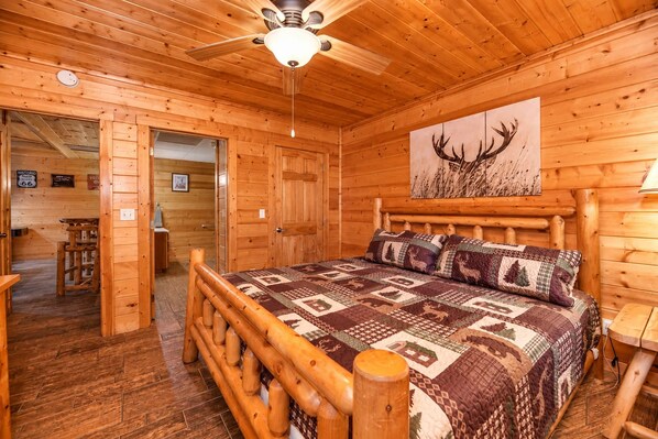 A wooden cabin bedroom with a bed, a ceiling fan, and a wall-mounted lamp.