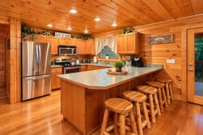 A wooden cabin kitchen with a stainless steel refrigerator, a microwave, a coffee maker, and a bar area with stools.
