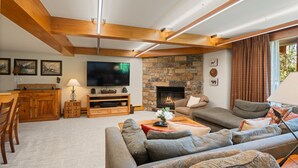 A spacious living room with a stone fireplace, wooden beams, a flat-screen TV, and a comfortable seating area. - Ski-in/ski-out directly from unit, 4 Bdrm DLX, Stonebridge Condos #925 (Snowmass Village)