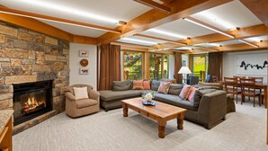 A spacious living room with a stone fireplace, a sectional sofa, a wooden coffee table, and a dining area with a table and chairs. - Ski-in/ski-out directly from unit, 4 Bdrm DLX, Stonebridge Condos #925 (Snowmass Village)