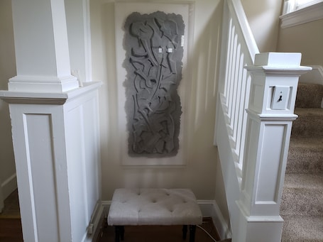 A hallway with a white bench, a decorative wall piece, and a staircase with white railings.