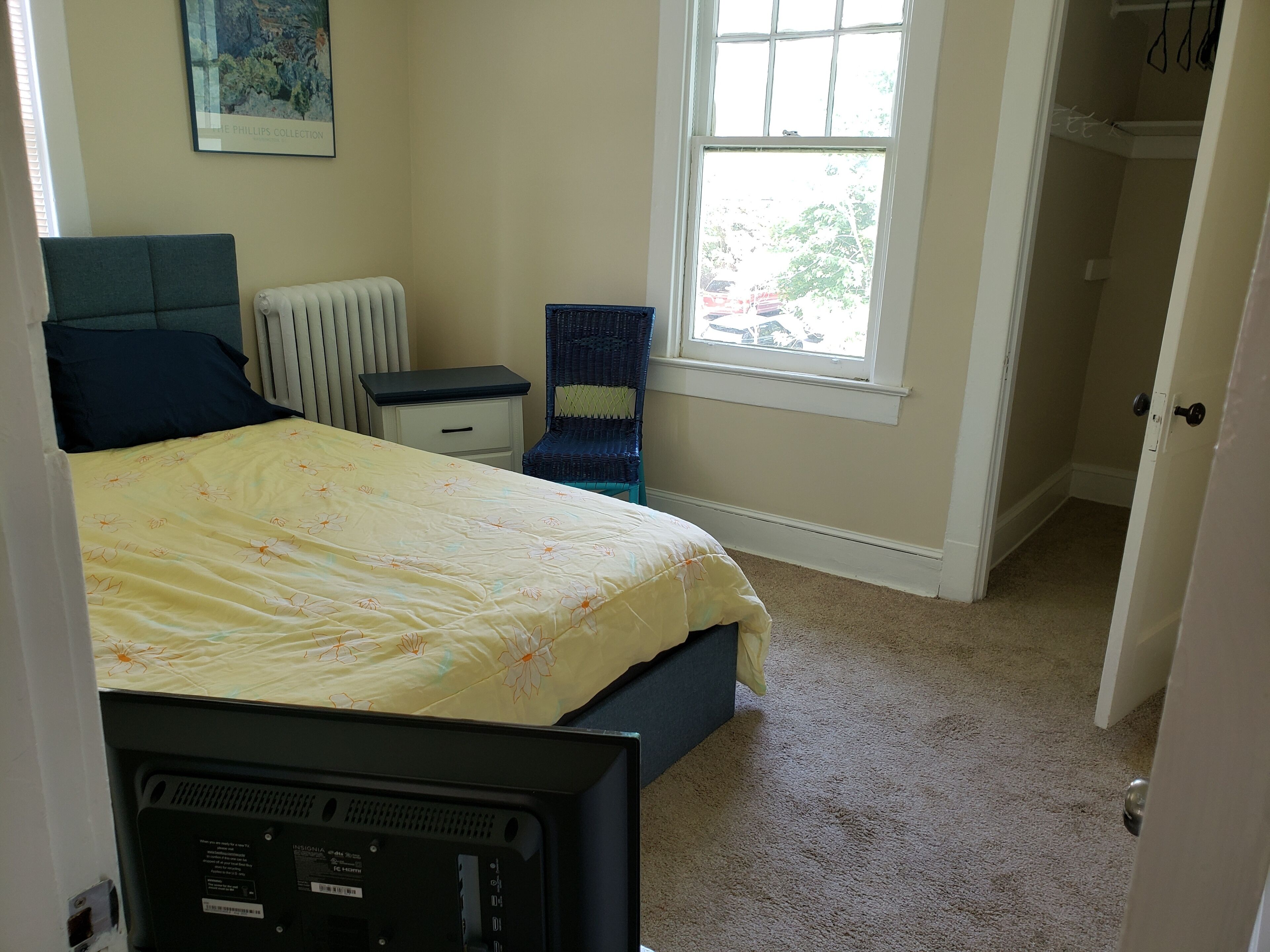 Une chambre à coucher avec un lit, une chaise, un radiateur, une fenêtre et une porte.