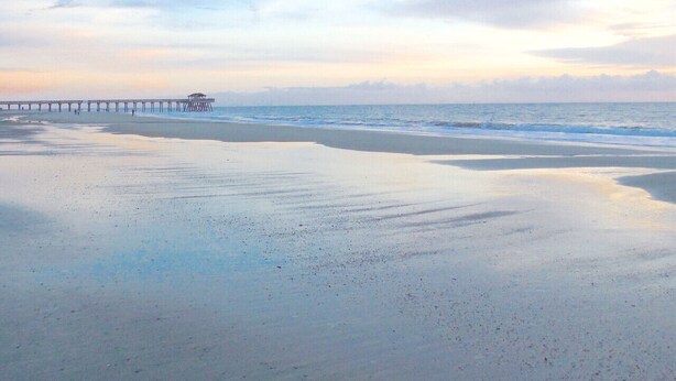 Ein Strand mit einem Steg, der ins Meer hinausführt.