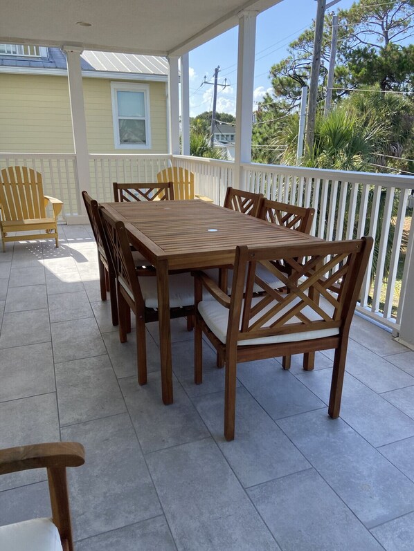 A covered patio with a wooden table and chairs, a white railing, and a view of a house and trees. - Tybee Retreat Unit 4 (Tybee Island)