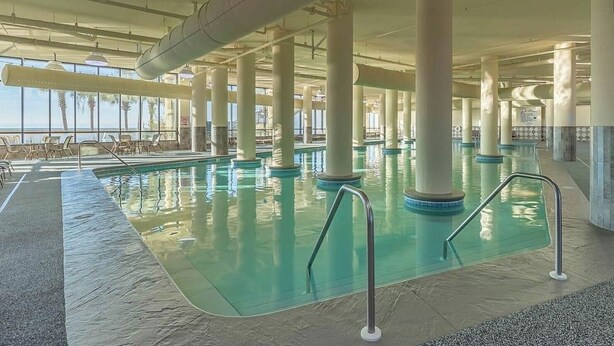 Ein Innenpool mit klarem Wasser, umgeben von Säulen und Liegestühlen.