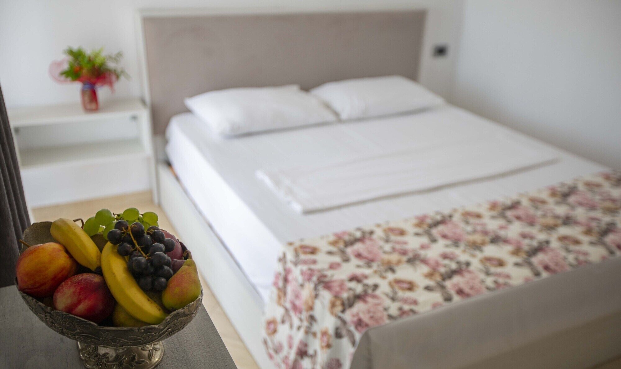 Un letto ben rifatto con lenzuola bianche e copripiumino a motivi floreali.