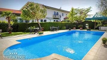 A swimming pool with a tiled deck, surrounded by a well-maintained garden and a building with balconies.