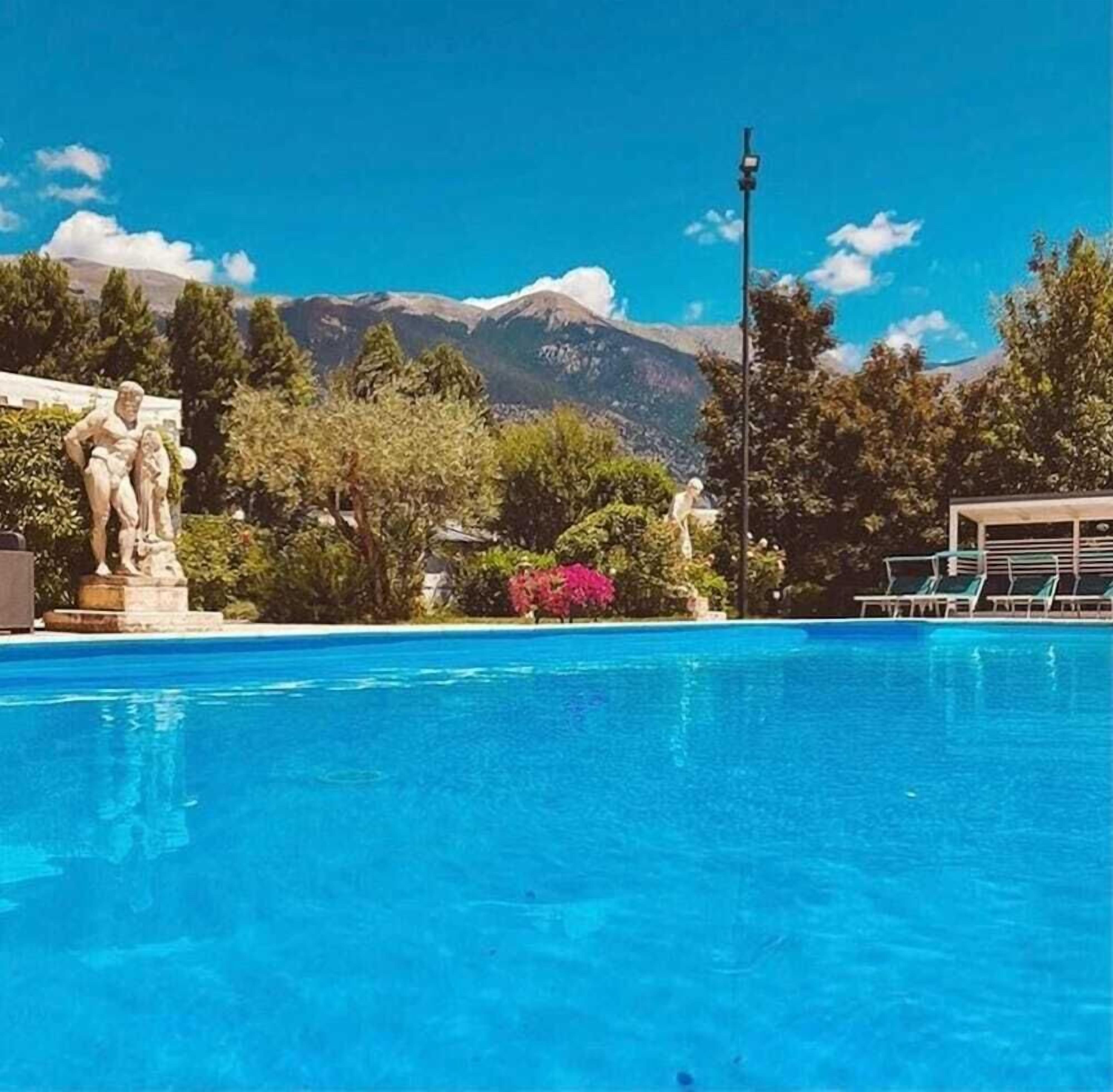 A swimming pool with a statue in the foreground, surrounded by trees and a mountain in the background.