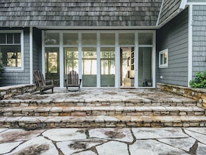 Step into this single-story home with a patio area featuring a glass door entrance and a cozy Adirondack chair.
