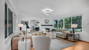 Un salon moderne avec un canapé, des fauteuils, une table basse et, au fond, un coin repas.