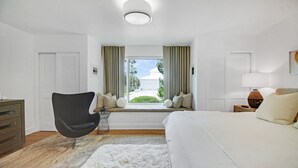 Une chambre à coucher avec un grand lit, une chaise, une fenêtre avec des rideaux et une vue sur l’extérieur.