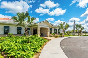 A building with a curved driveway, palm trees, and a clear blue sky.