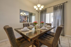 Un comedor con una mesa larga dispuesta para seis comensales, rodeada de sillas tapizadas, un candelabro y un espejo grande sobre la mesa.