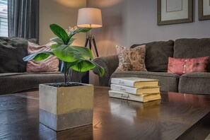Una sala de estar con una mesa de centro de madera, una planta en maceta, una lámpara de pie y una pila de libros sobre la mesa.
