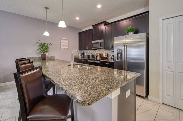 A modern kitchen with granite countertops, stainless steel appliances, and dark cabinetry. - 3111 - Mickeys Hideaway - Water park Included (Kissimmee)