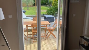 Una habitación con puerta de vidrio corredera que da a un patio al aire libre con mesa y sillas de madera, una parrilla y un paraguas cubierto.