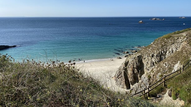 Una playa costera con terreno rocoso y una escalera de madera que baja hacia la orilla.