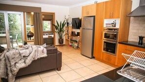 Eine moderne Küche mit Holzschränken, einem Edelstahlkühlschrank und einem eingebauten Backofen. Es gibt eine Essecke mit Tisch und Stühlen, sowie ein großes Fenster für natürliches Licht.