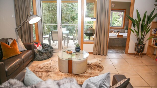 Ein modernes Wohnzimmer mit einer Ledersofa, einem Glastisch und einem Fellteppich. Durch Glastüren ist ein Essbereich mit Tisch und Stühlen erkennbar.