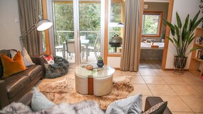 Ein modernes Wohnzimmer mit einer Ledersofa, einem Glastisch und einem Fellteppich. Durch Glastüren ist ein Essbereich mit Tisch und Stühlen erkennbar.