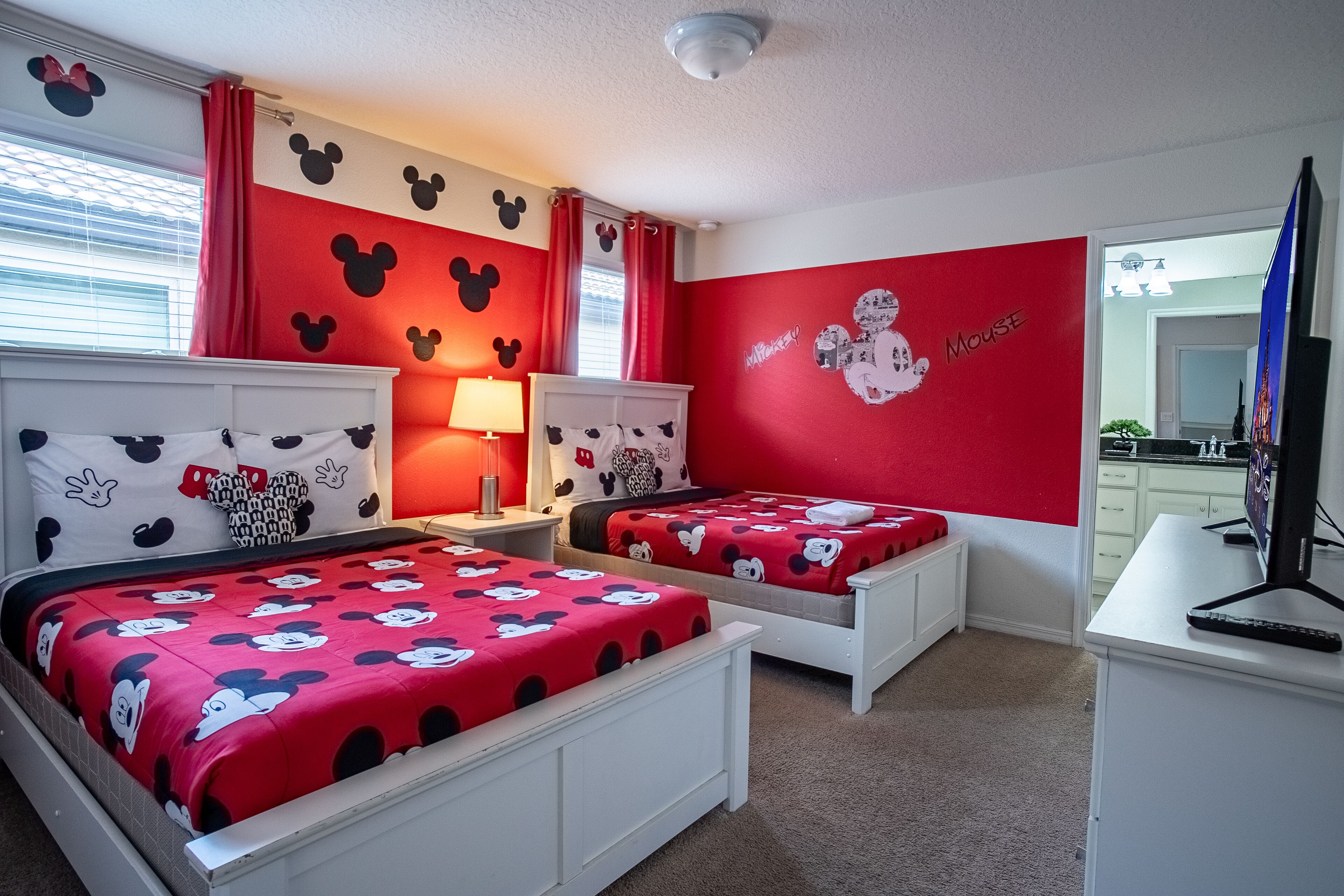 A bedroom with two beds, red and white walls, and Mickey Mouse decorations.