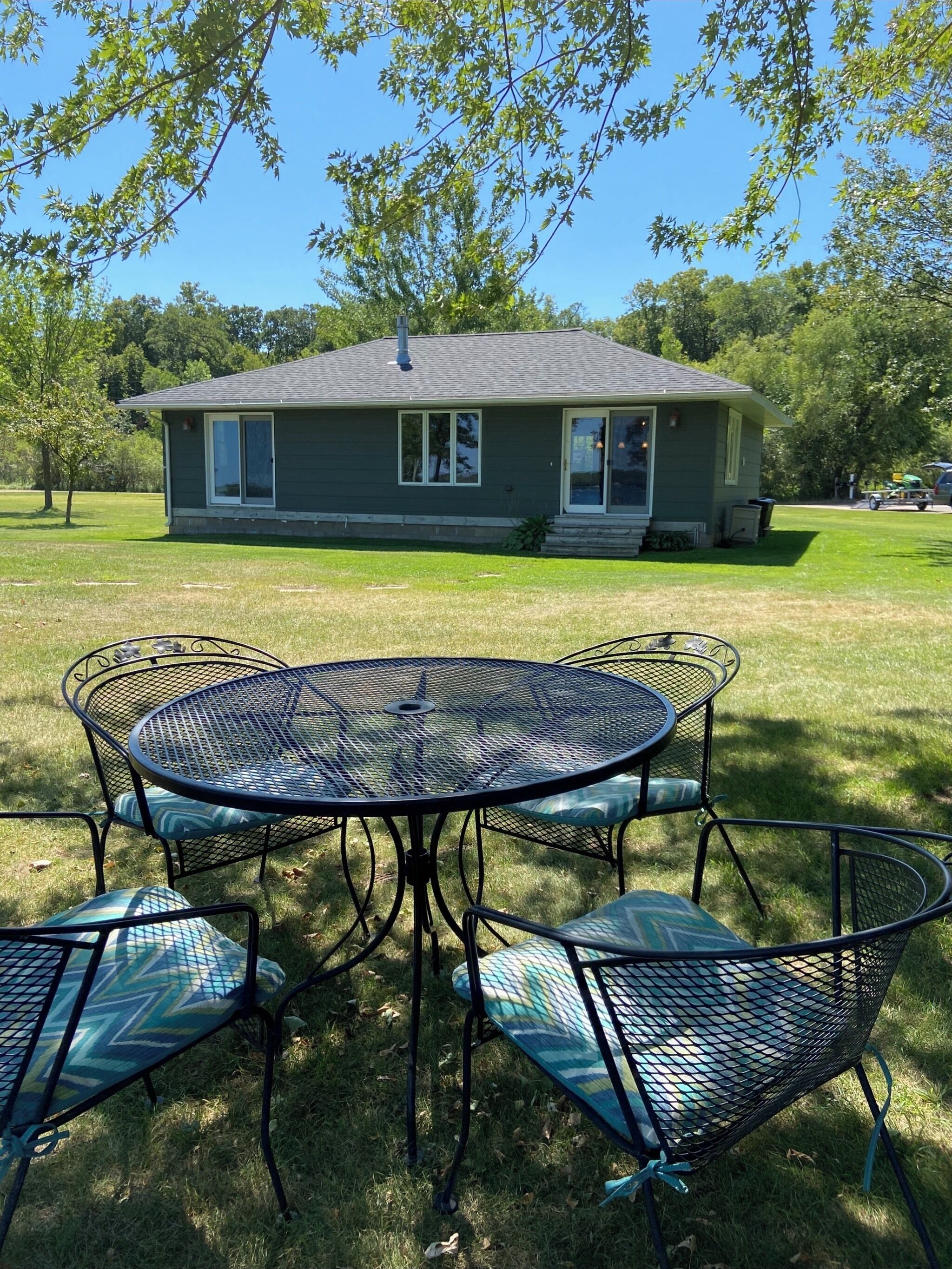 Une maison avec une pelouse et une table en métal entourée de chaises.