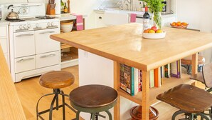 Une cuisine avec des appareils électroménagers blancs, des tabourets en bois, un îlot central et divers ustensiles de cuisine.