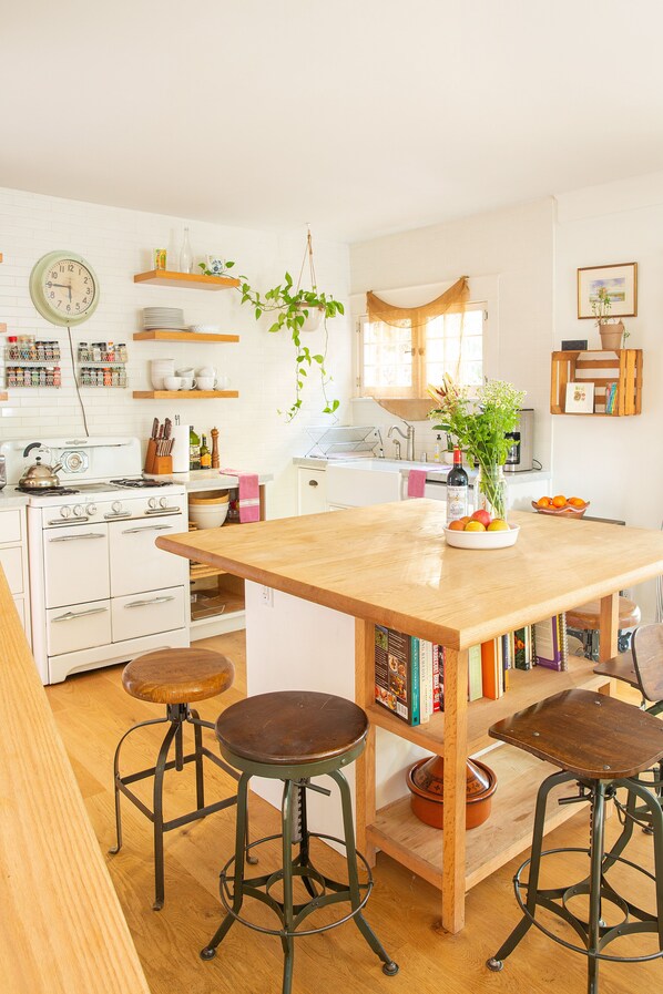 A kitchen with white appliances, wooden stools, a central island, and various kitchen items.