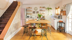 Une cuisine avec une table en bois, des tabourets de bar, un four à micro-ondes et divers ustensiles de cuisine rangés sur des étagères.