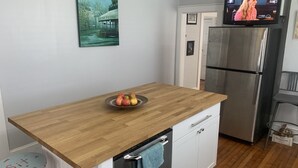 A kitchen with a wooden countertop, a bowl of fruit, a stainless steel refrigerator, a television, and a framed picture on the wall. - This bungalow is 5 min from downtown the riverfront and 12 min from the beach! (wilmington)