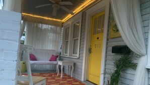 A porch with a yellow door, a white bench, a small table, and a potted plant. - This bungalow is 5 min from downtown the riverfront and 12 min from the beach! (wilmington)