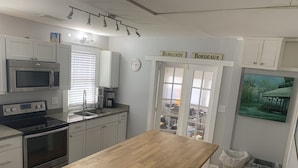 A kitchen with white cabinets, a wooden countertop, and a view of the street through a door. - This bungalow is 5 min from downtown the riverfront and 12 min from the beach! (wilmington)
