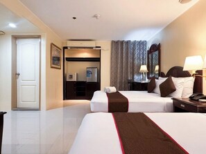 A hotel room with two beds, a desk, a chair, a refrigerator, and a door. - Palladium Suites (Cebu City)