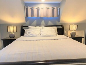 Quarto com uma cama grande, duas mesas de cabeceira com luminárias e uma janela com cortinas.