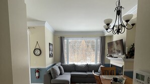 Ein Wohnzimmer mit einem Ecksofa, einem Esstisch mit Stühlen, einer Pendelleuchte und einem Kamin.