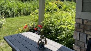 Ein Holztisch mit einem Glasbehälter auf einer Veranda mit Blick auf einen üppigen Garten und Wald.