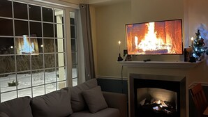 Ein Wohnzimmer mit einem großen Flachbildfernseher über einem Kamin, einem Ecksofa und Blick auf eine verschneite Landschaft durch ein großes Fenster.