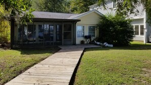 A house with a covered patio, a lawn, and a wooden deck leading to the entrance. - Pappy's Pool Lake: A  1650 sqft with Pier,  Boat Ramp, Screened porch,Lakeside. (Lake Waccamaw)