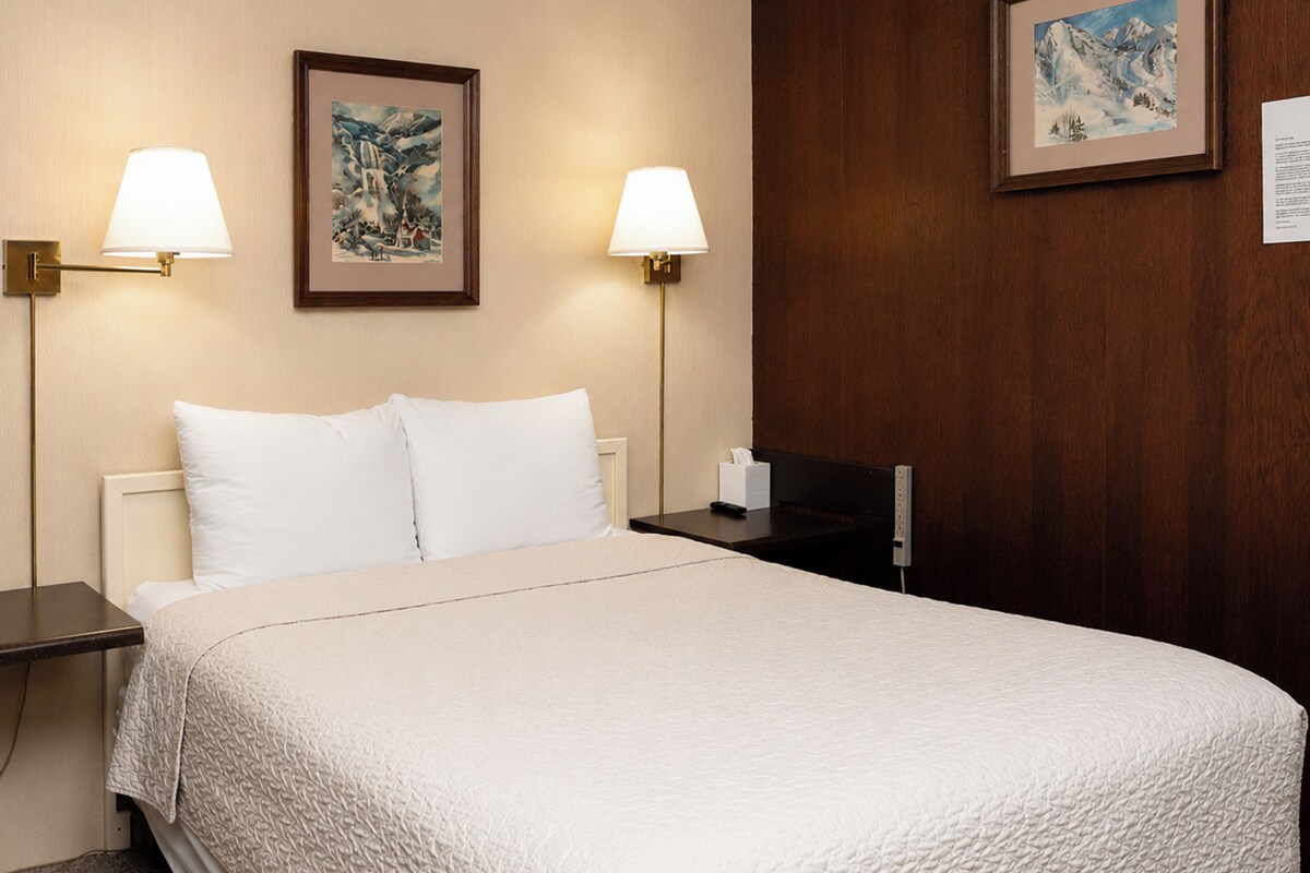 A hotel room with a bed, two bedside tables, two wall-mounted lamps, and two framed pictures on the wall.