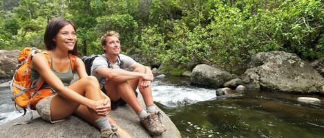 Twee personen zitten op een rots langs een stromende rivier, omgeven door groen.