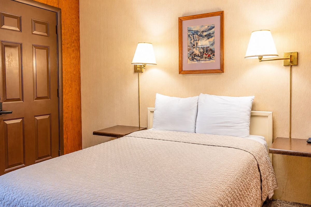 Ein Hotelzimmer mit einem Bett, zwei Nachttischen, einer Tür und zwei Wandlampen.