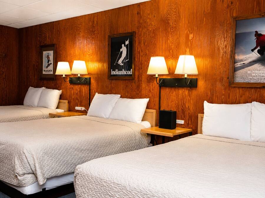 Habitación de hotel con dos camas, paneles de madera en las paredes y lámparas fijadas a la pared.