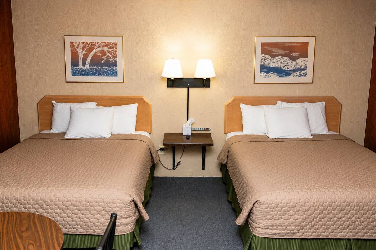 Ein Hotelzimmer mit zwei Betten, einem Nachttisch, einer Lampe und zwei gerahmten Bildern an der Wand.