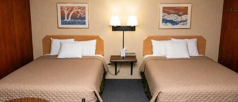 A hotel room with two beds, a nightstand, a lamp, and two framed pictures on the wall.