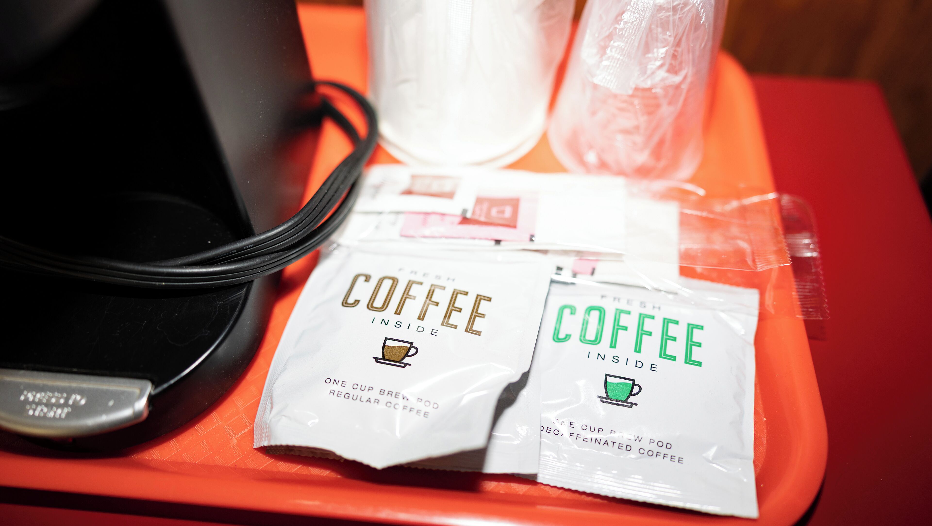 Dispensador de cápsulas de café con dos cápsulas, una etiquetada 'Café Fresco Adentro' y la otra 'Descafeinado, Café Sin Cafeína'.
