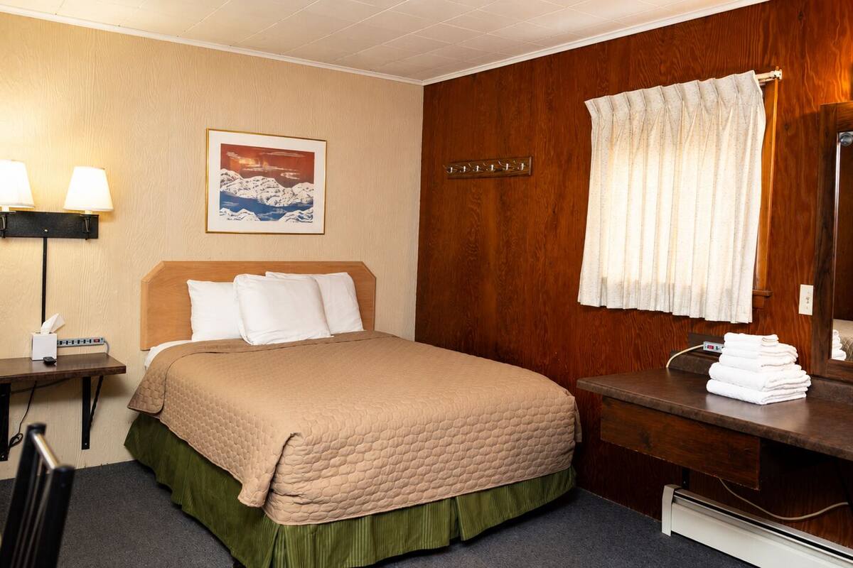Ein Hotelzimmer mit Bett, Nachttisch, Lampe, Spiegel und einem gerahmten Bild an der Wand.