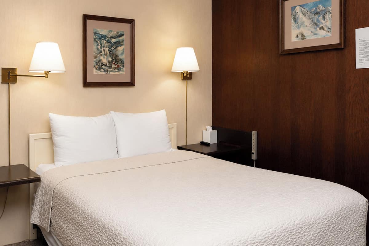 Ein Hotelzimmer mit einem Bett, zwei Nachttischen, zwei Wandlampen und zwei gerahmten Bildern an der Wand.