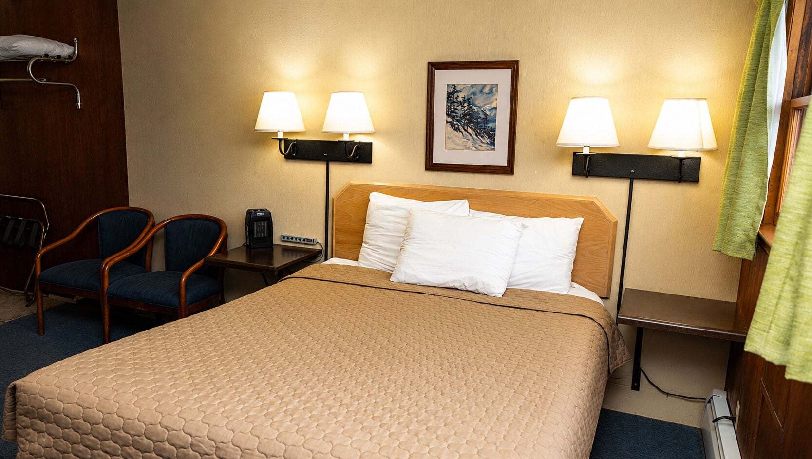 Een hotelkamer met een bed, twee stoelen, een nachtkastje, een lamp en een schilderij aan de muur.